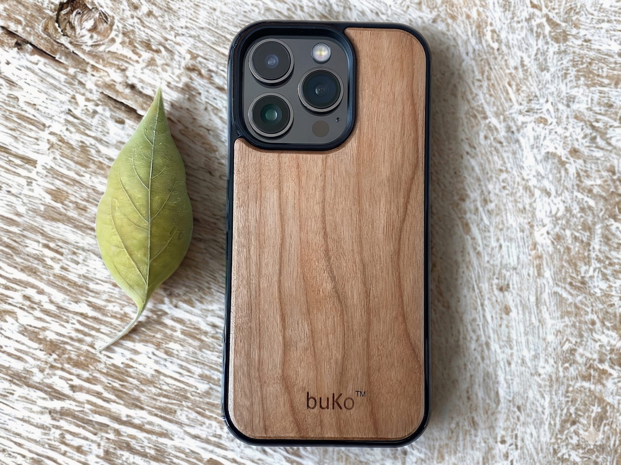 Buko natural wood iPhone case with slim black bumper on rustic timber surface with leaf