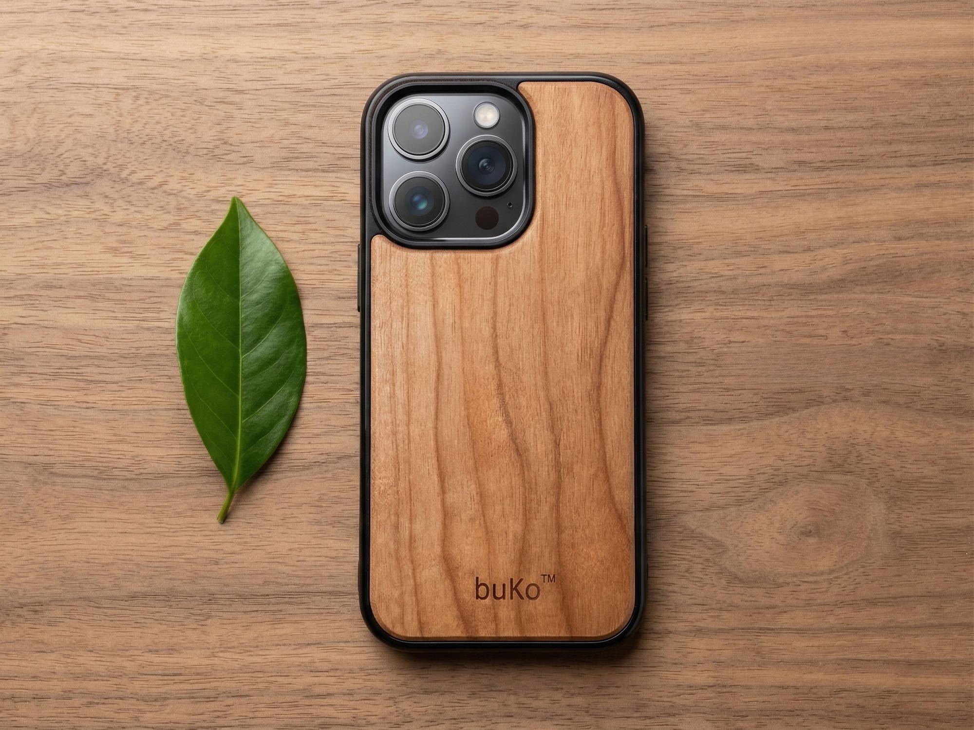 buko wooden phone case on walnut wood table with green leaf beside it