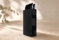 Black BuKo leather double pop-up card wallet with stacked cards on a warm neutral rustic style background.