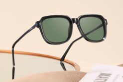 SoCal black acetate sunglasses with green polarised lenses displayed on a mirror and magazine.