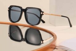 SoCal black sunglasses with gold metal arms and grey polarised lenses displayed on a mirrored surface.