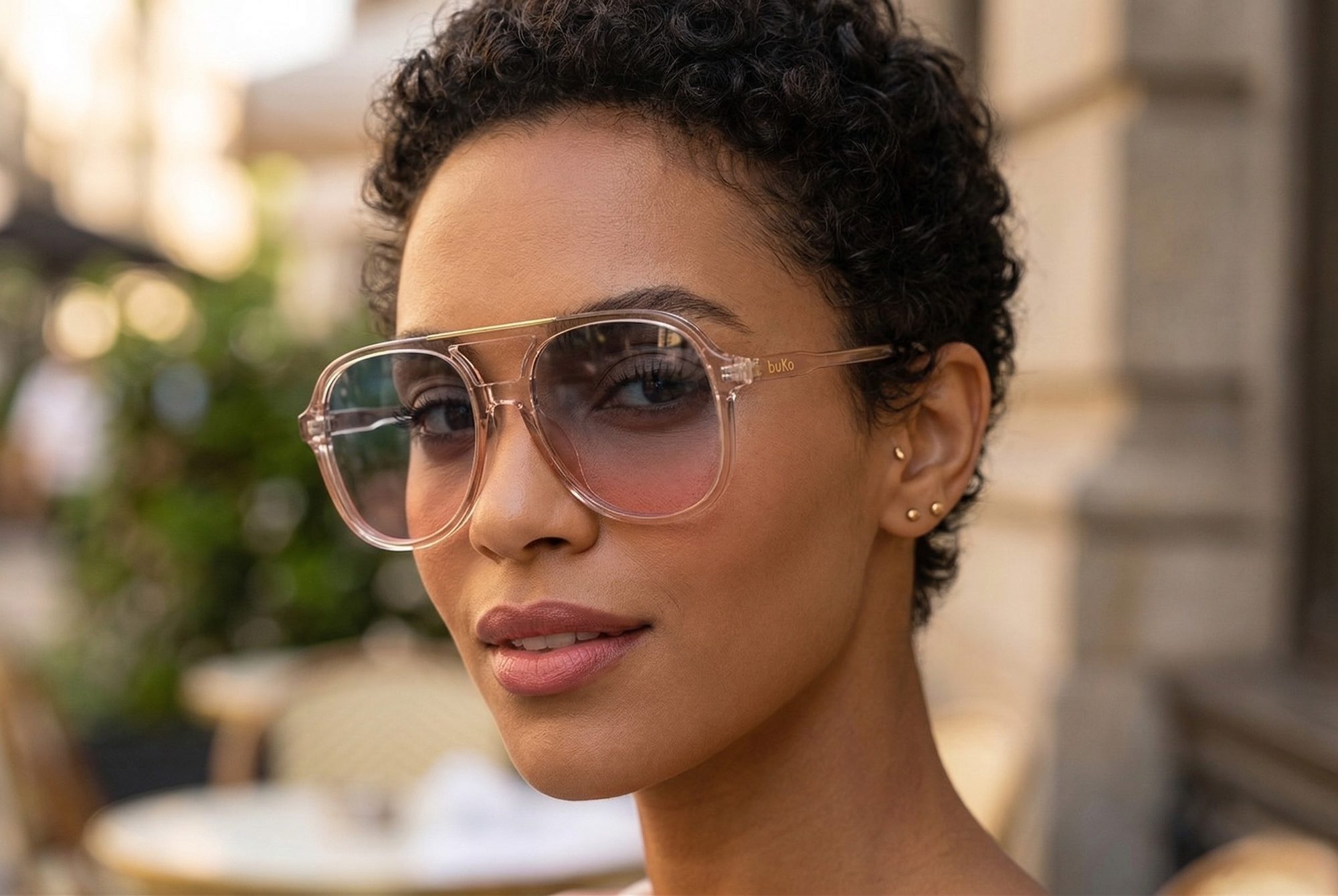 Female model wearing Buko Wategos sunglasses in transparent pink acetate frame with gradient lenses, retro aviator style with arched double bridge