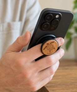 Person holding a black iPhone using the buKo MagSafe Phone Holder & Stand with engraved wooden turtle design